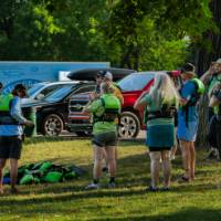 group putting on life jackets on grass next to a paved parking lot